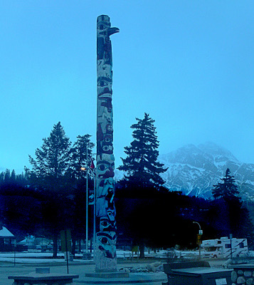 [Totum pole is probably at least 20 feet high and has a series of faces one on top of the other. The face at the top has a beak like a bird.]